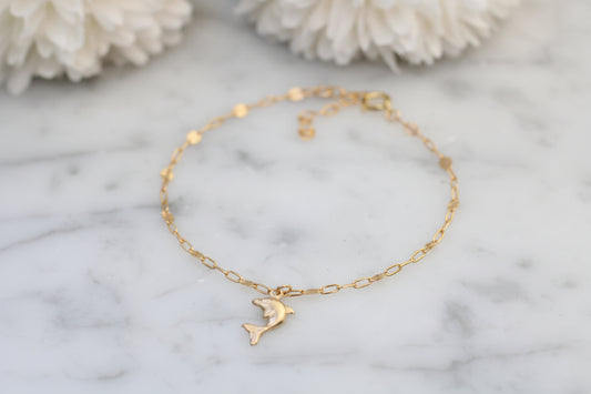 Gold anklet with a dolphin charm on a marble surface