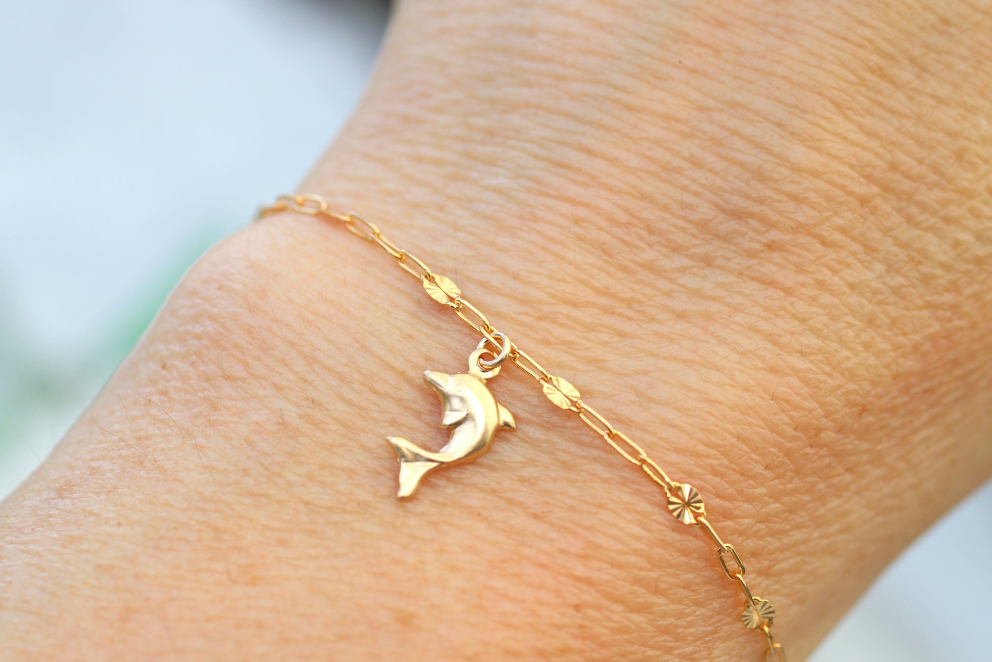 Gold bracelet with a dolphin charm on a wrist against a light background