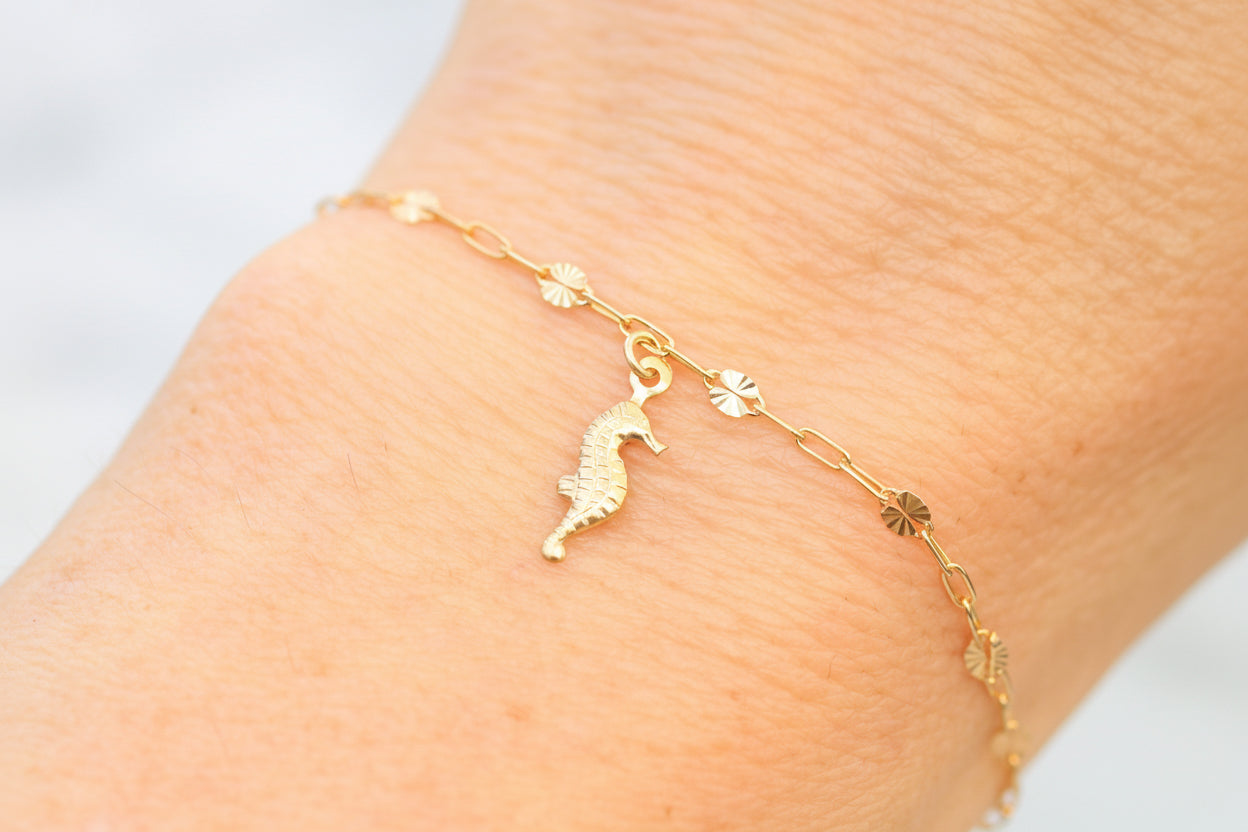 Gold bracelet with a seahorse charm on a person's ankle against a light background