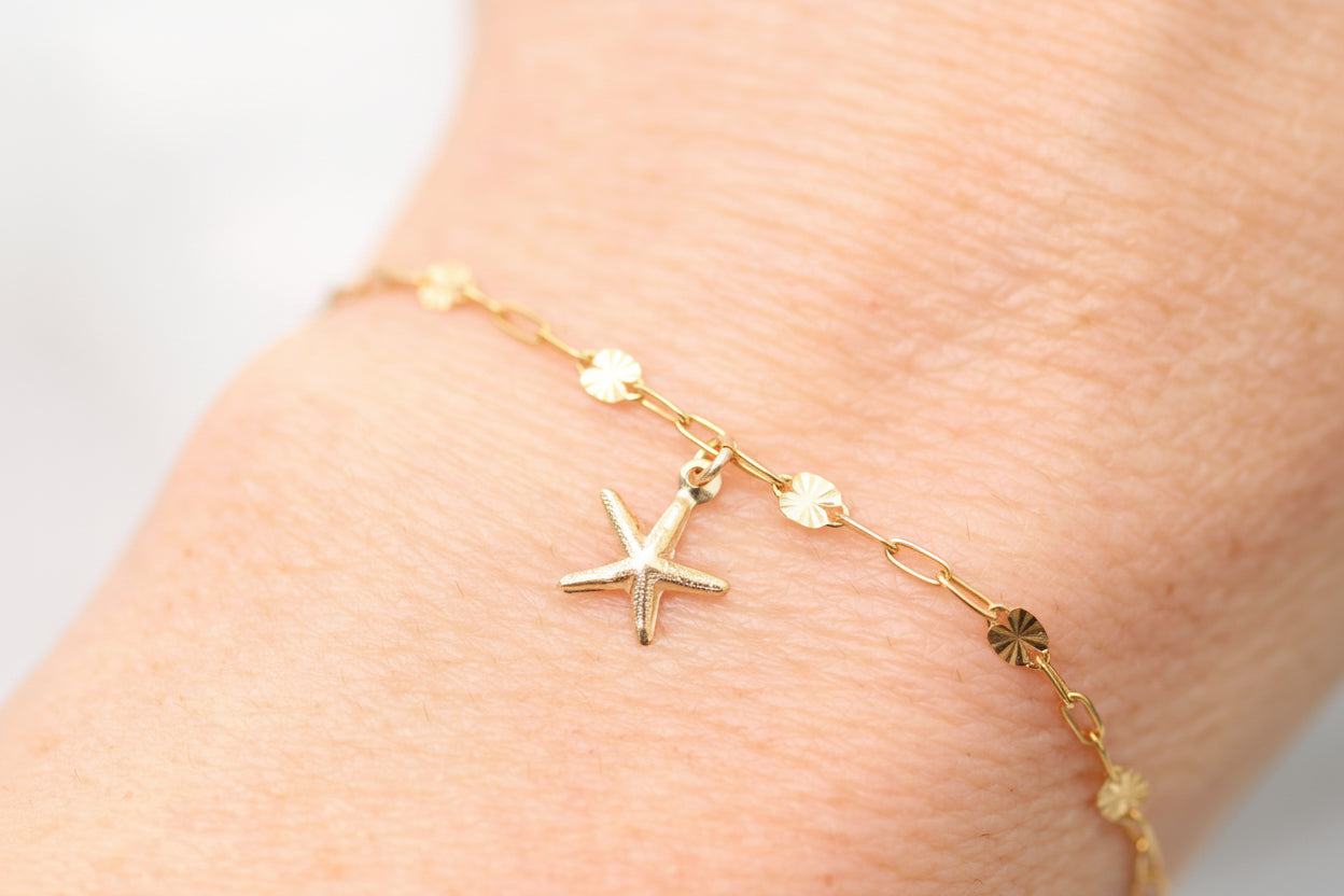 Gold bracelet with starfish charm on a wrist against a neutral background