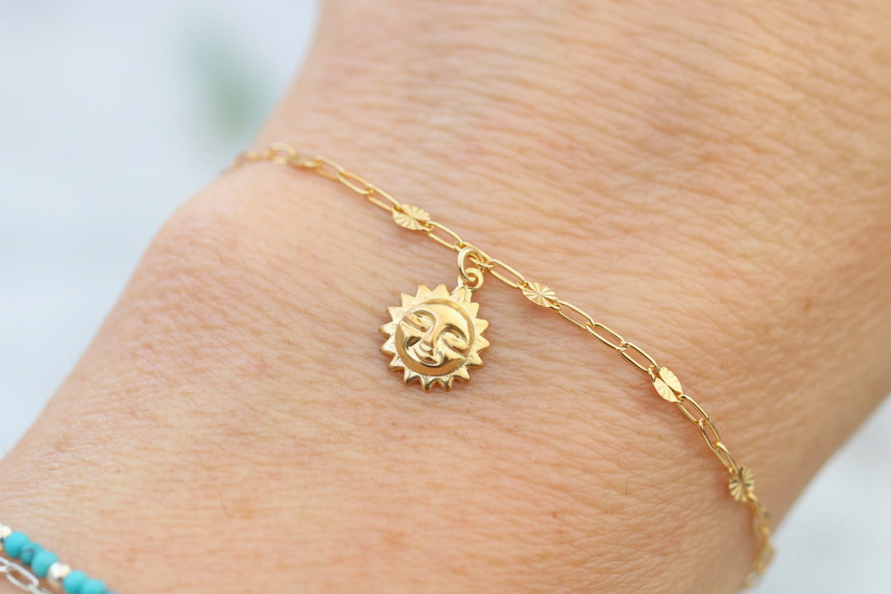 Gold bracelet with sun charm on a wrist against a light background