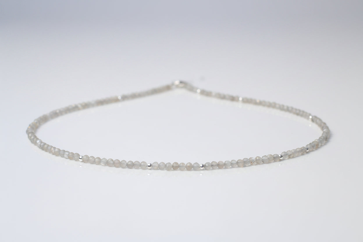 A grey moonstone choker necklace with sterling silver setting, featuring a series of round beads strung on a chain.