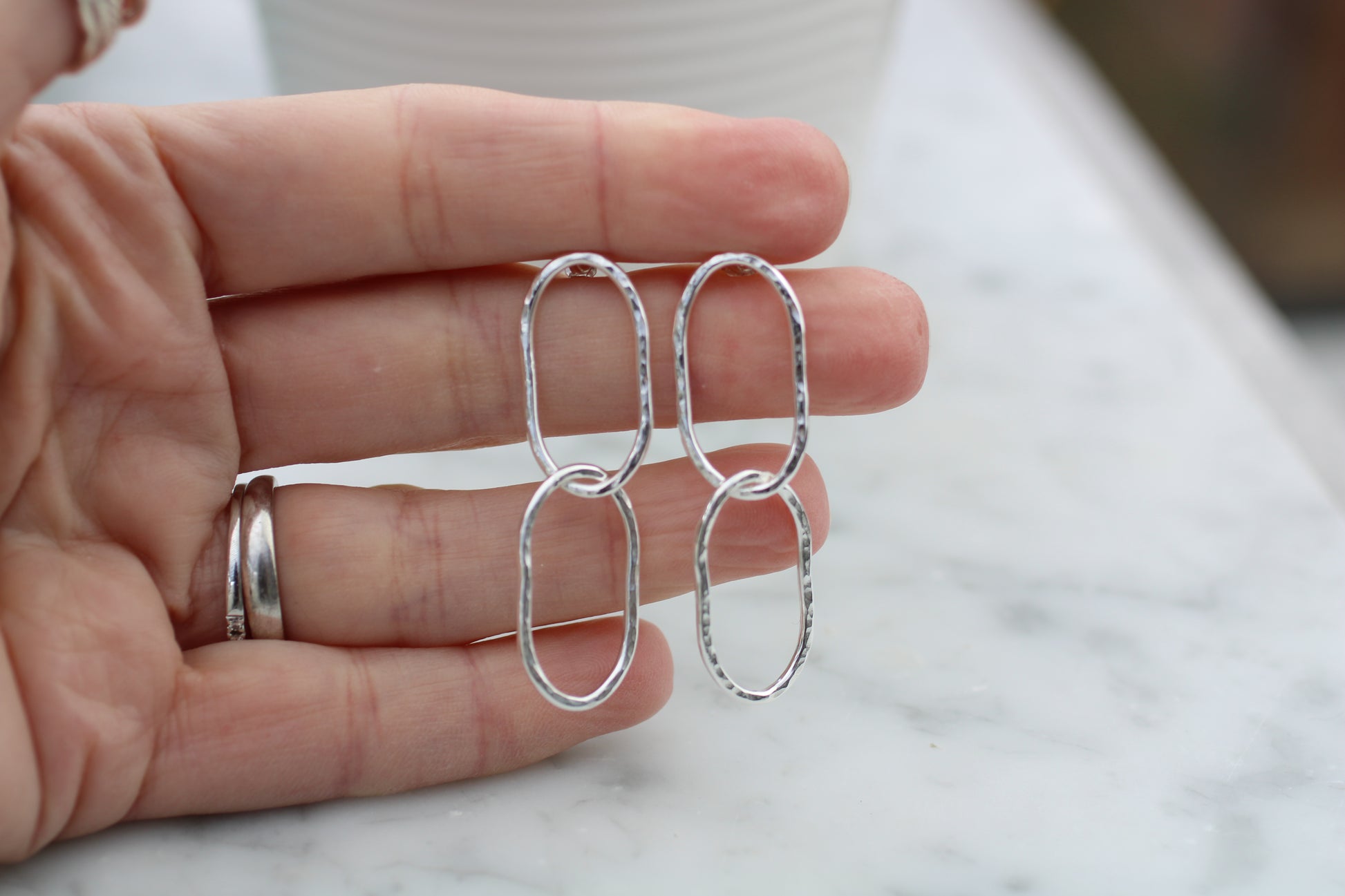 Silver earrings held between fingers on a marble surface