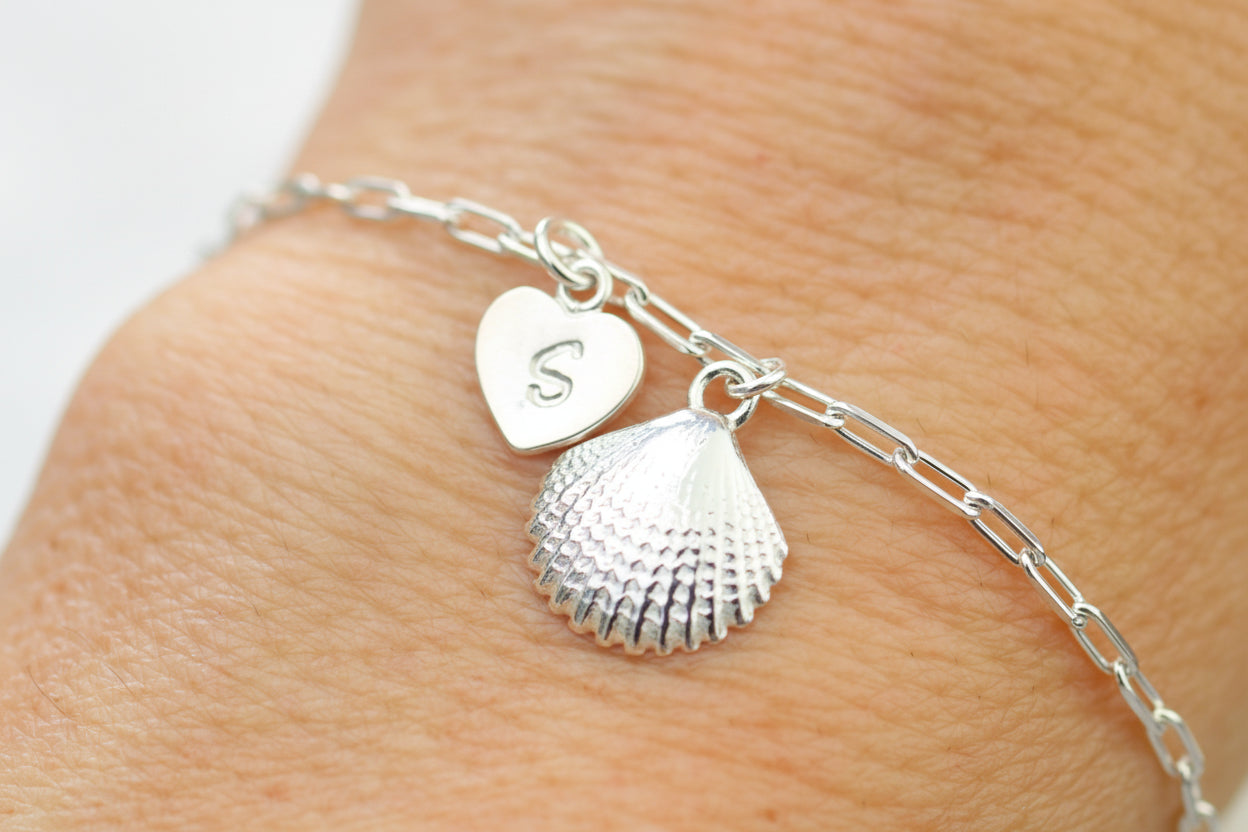 Silver bracelet with heart and shell charms on a wrist