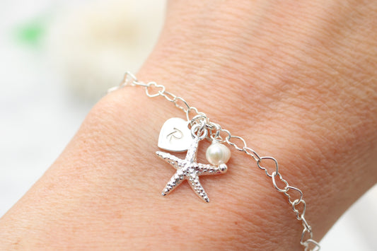 Silver braeclet with starfish and pearl charm on a person's ankle against a blurred background