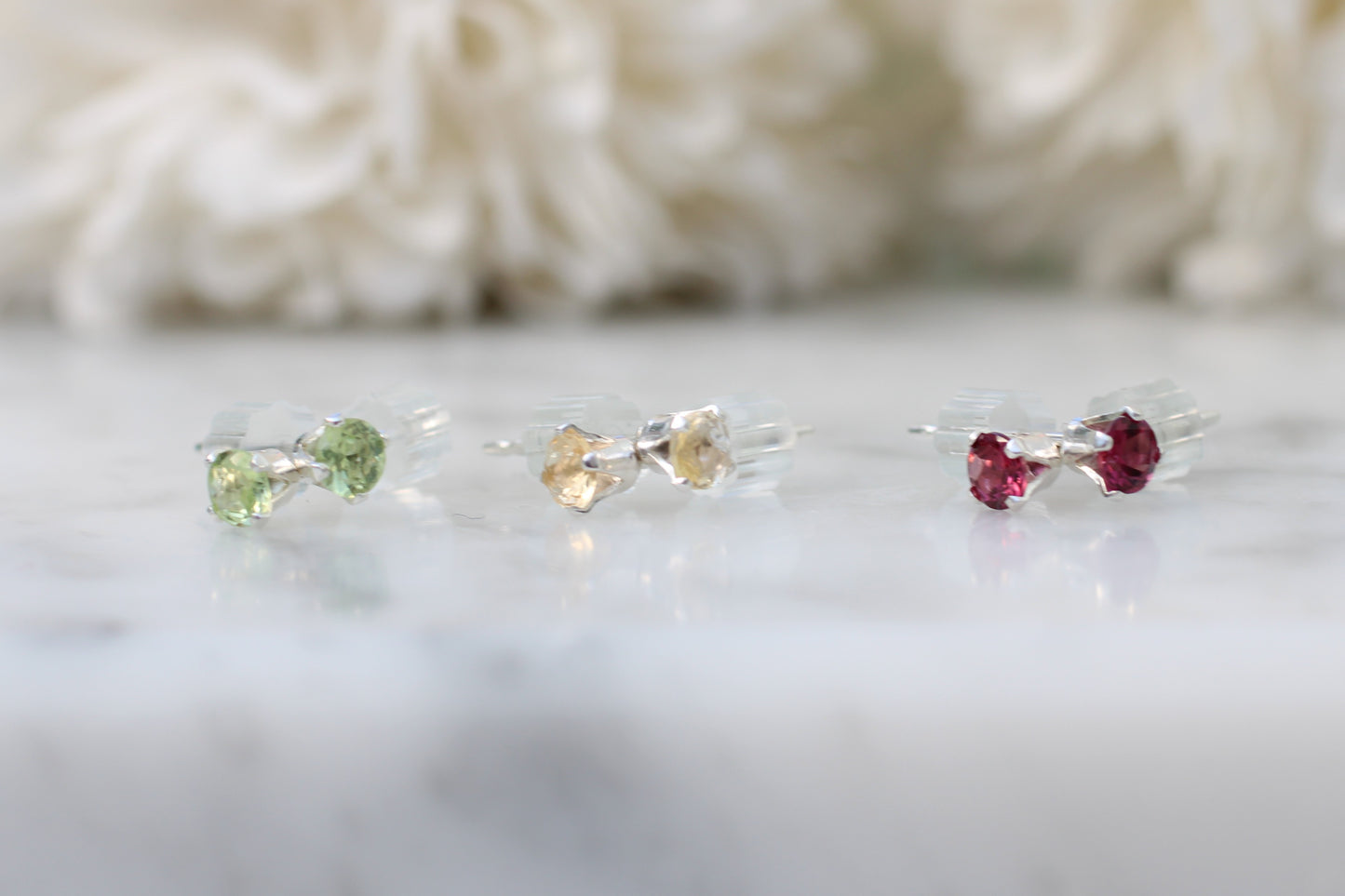 Three small gemstone earrings on a white surface with a blurred background