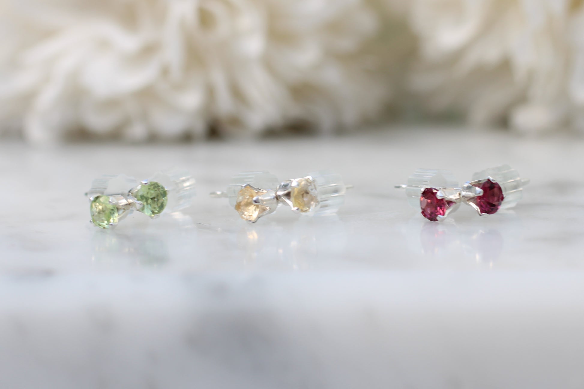 Three small gemstone earrings on a white surface with a blurred background