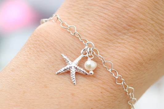 Silver bracelet with starfish and pearl charm on wrist against a blurred background