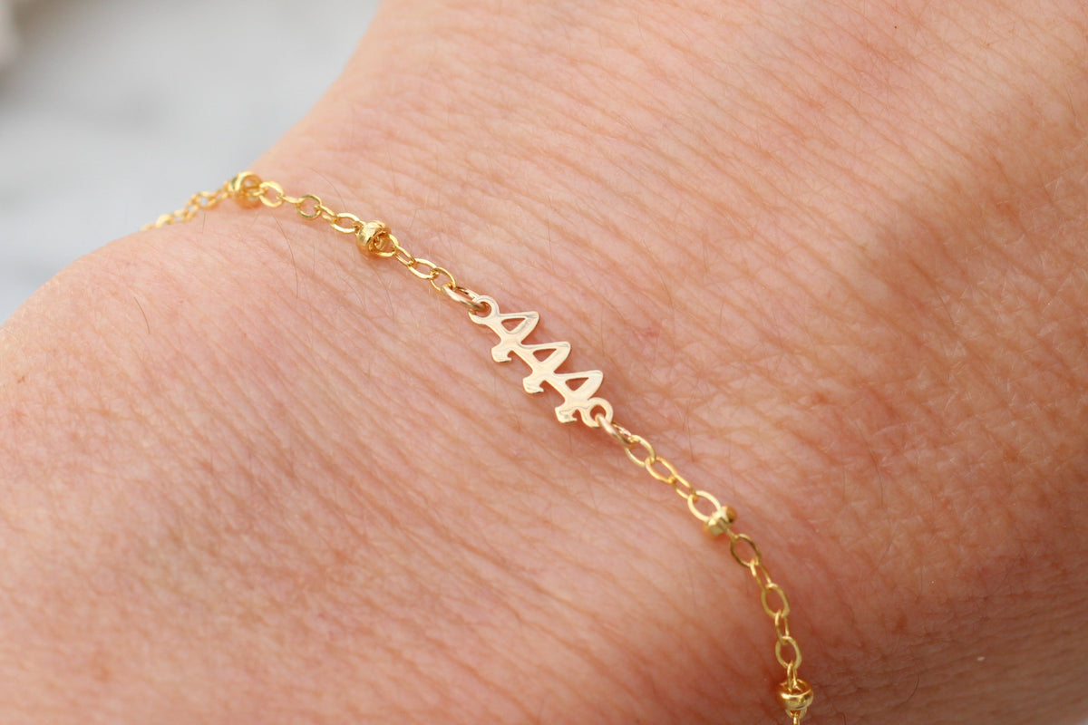 A delicate gold chain bracelet with a personalized nameplate spelling '444' in a cursive font, shown worn on a person's wrist.
