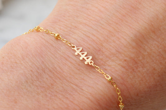 A delicate gold chain bracelet with a personalized nameplate spelling '444' in a cursive font, shown worn on a person's wrist.