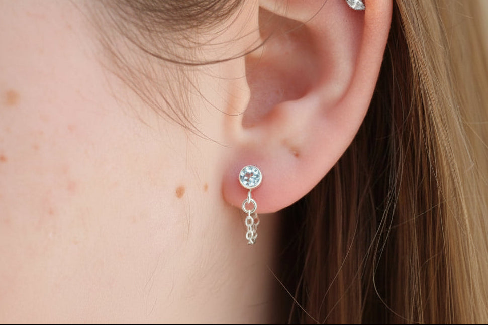 Close-up of a person's ear wearing two earrings with a blurred background