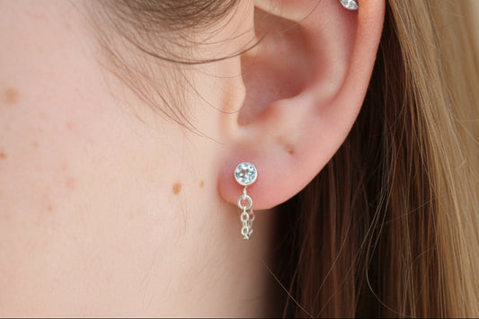 Close-up of a person's ear wearing two earrings with a blurred background