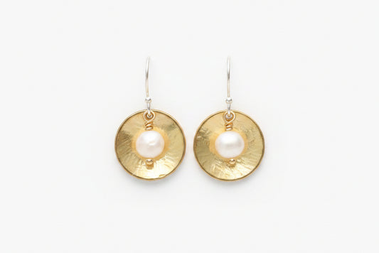A pair of gold and silver drop earrings featuring a textured circular gold disc with a white pearl at the center, suspended from silver hooks on a plain white background.