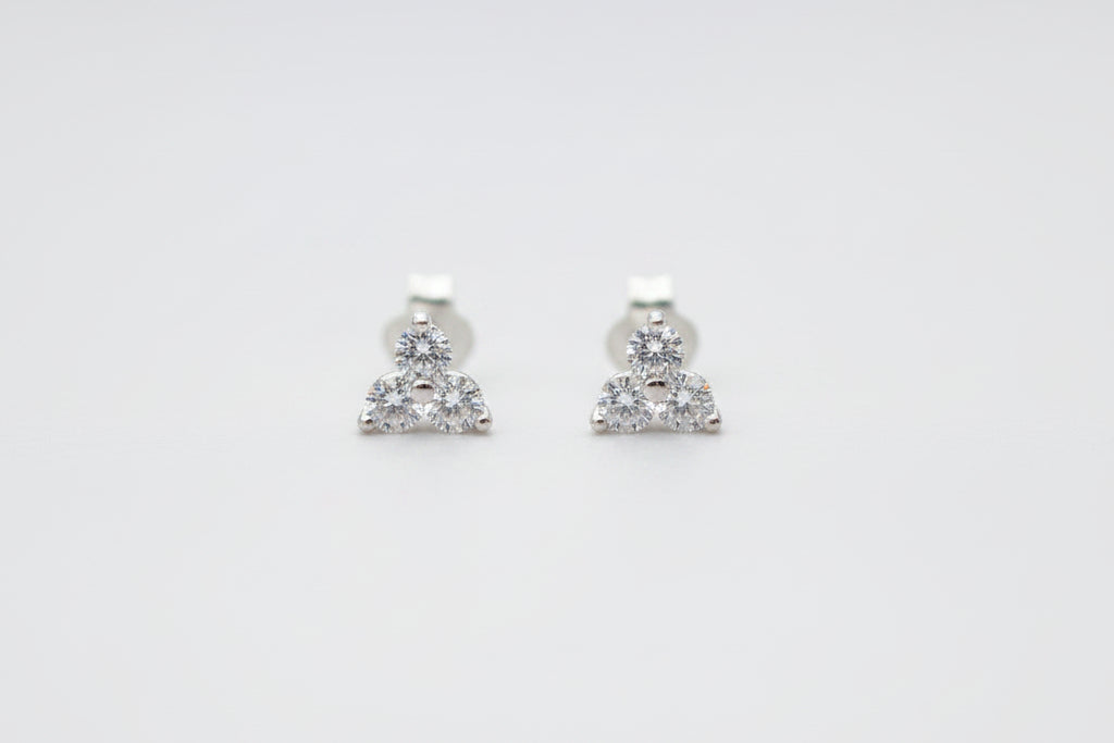 A pair of small silver stud earrings with three clear stones clustered at the bottom, resting on a light marble surface.