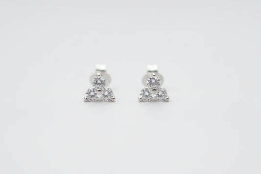 A pair of small silver stud earrings with three clear stones clustered at the bottom, resting on a light marble surface.