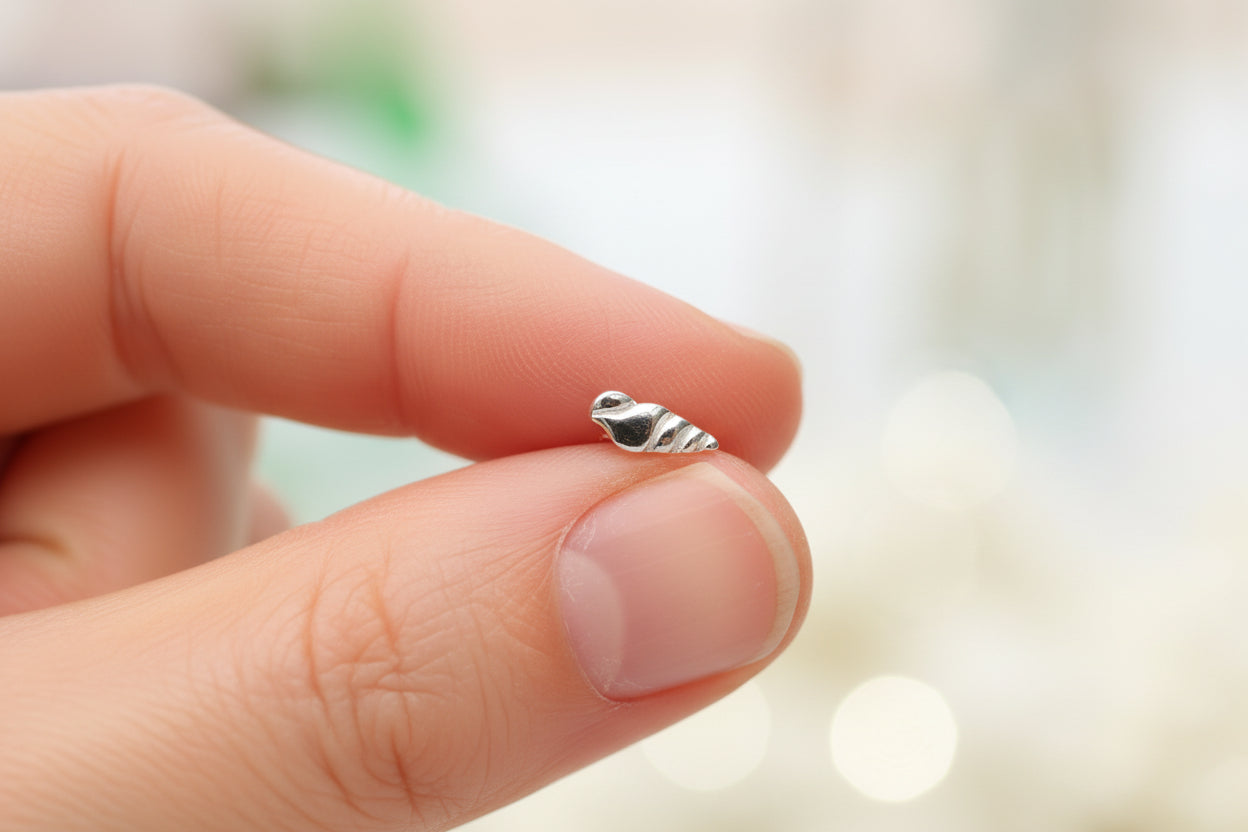 A tiny silver shell-shaped charm or bead resting on a person's fingers, shown in a close-up hand-held shot.