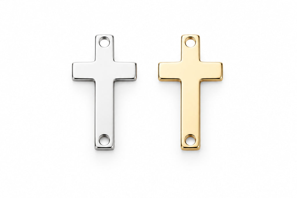 Two small flat cross charms, one silver-toned and one gold-toned, placed side by side on a white and gray marble surface.