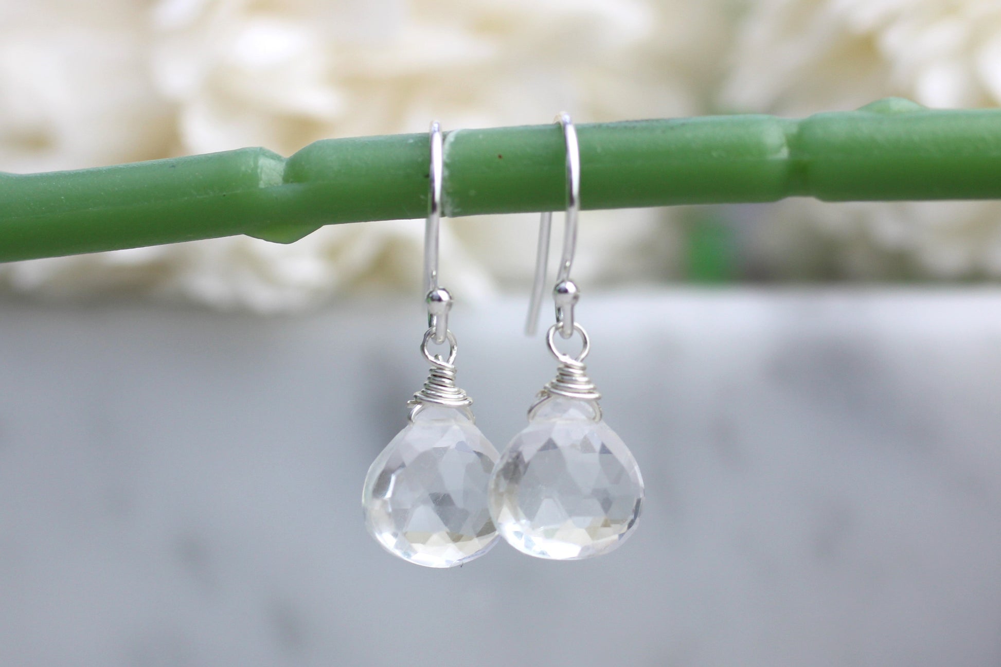 A pair of quartz earrings dangle from wire-wrapped settings, showcasing a clear gemstone finish, displayed on a green stem.