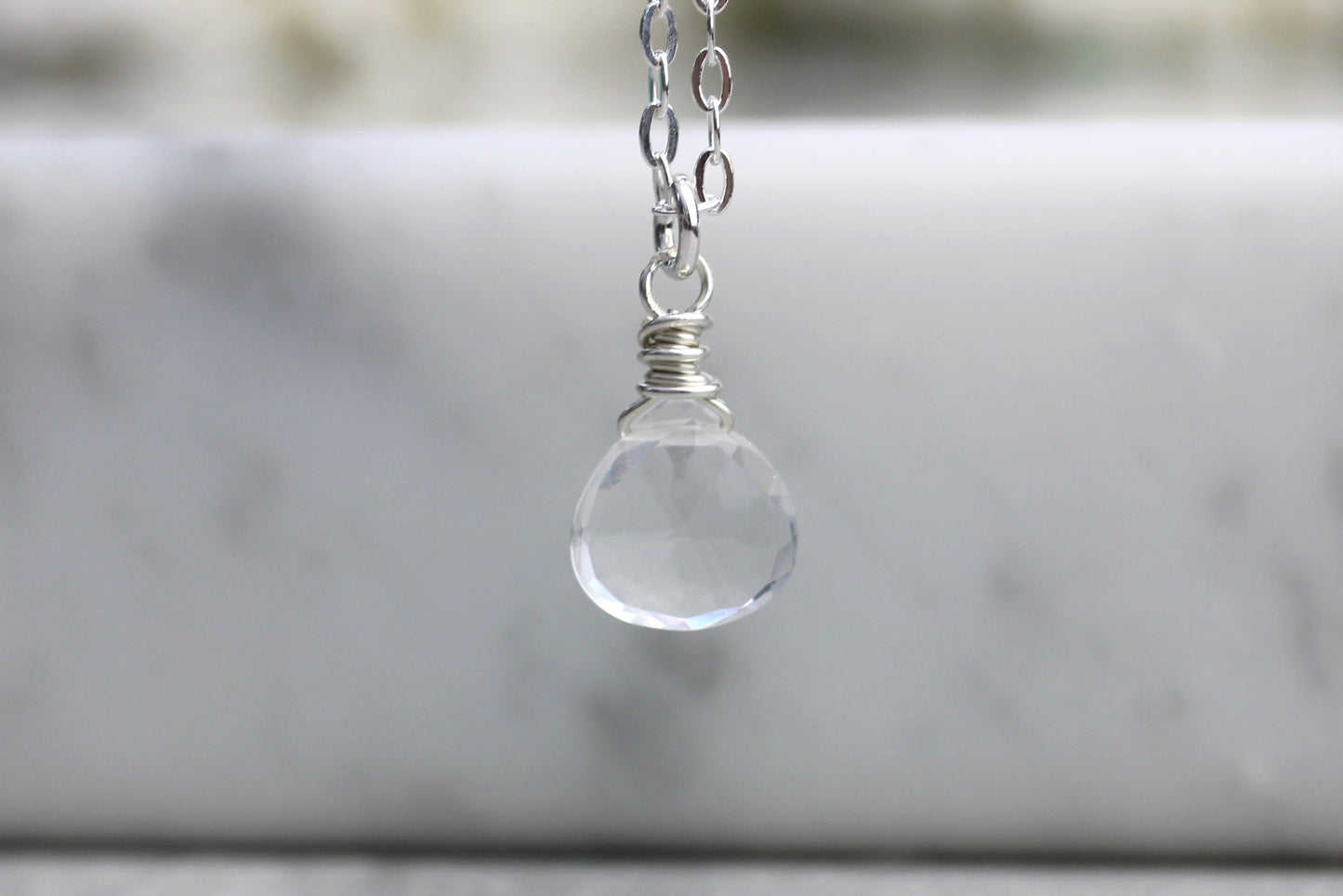 A clear quartz briolette gemstone necklace with a silver or gold-filled metal wire wrap, displayed against a marble background.