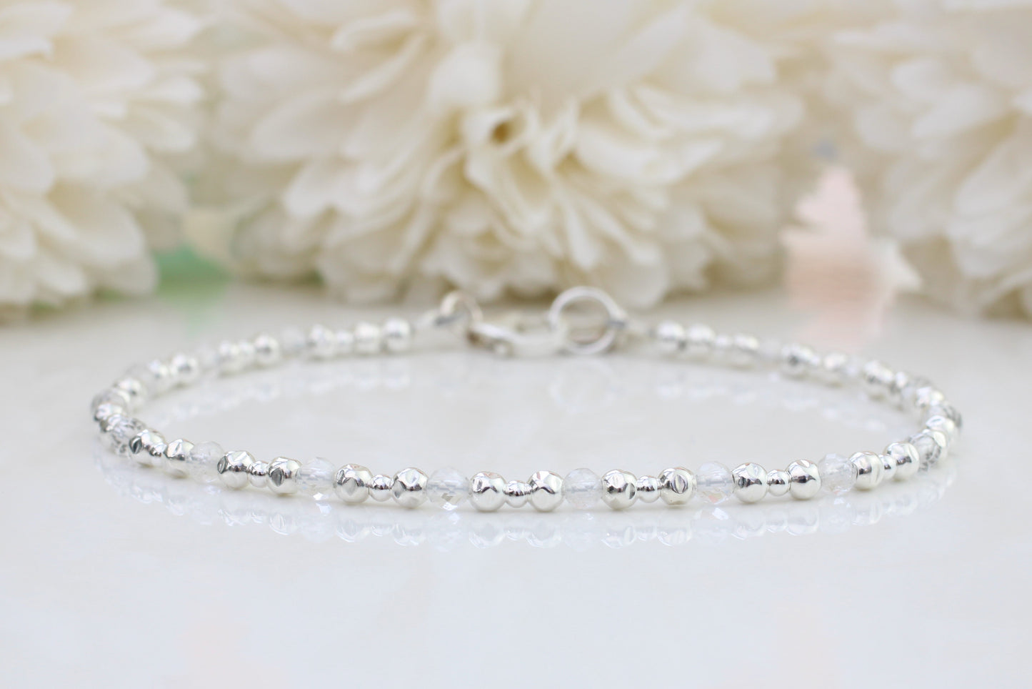A sterling silver bracelet with crystal quartz gemstones displayed against a floral background.