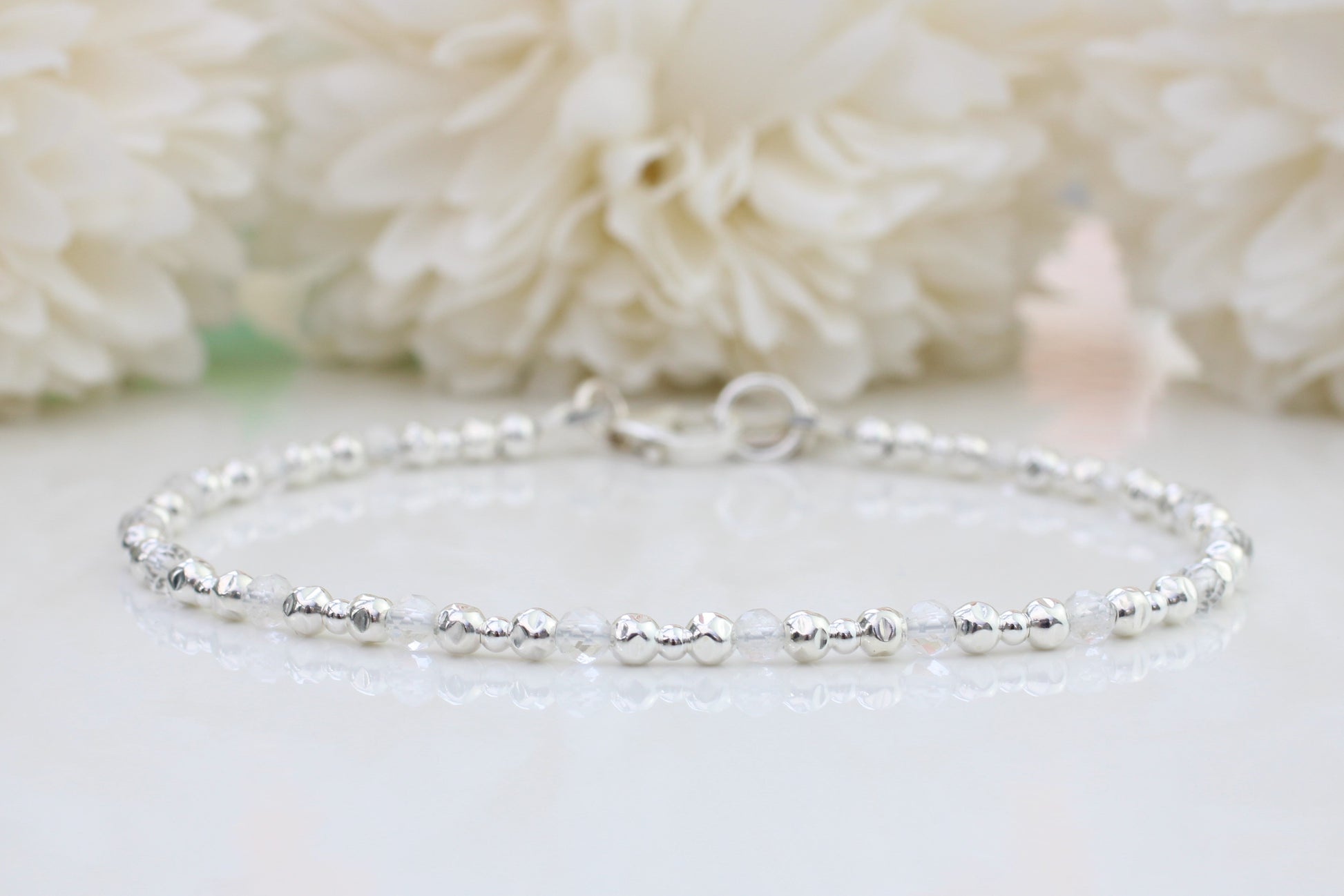 A sterling silver bracelet with crystal quartz gemstones displayed against a floral background.