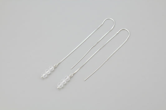 Silver earring threads with small beads on a gray background