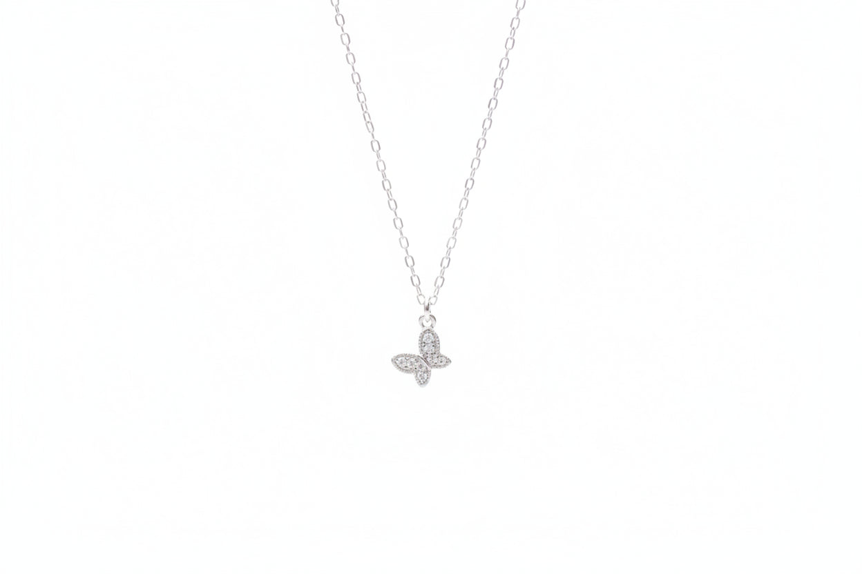 Silver butterfly necklace on a marble surface with white flowers in the background