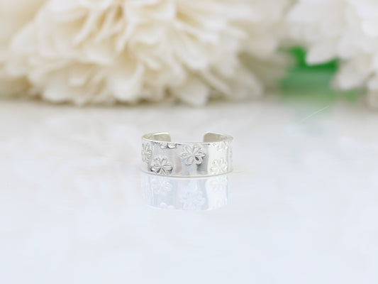 A silver ear cuff with a daisy pattern, placed on a white surface next to some white flowers.