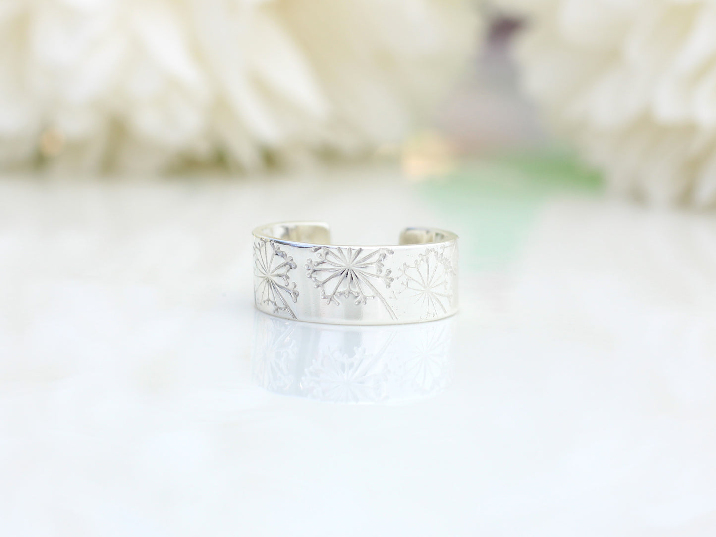 silver ear cuff with a dandelion design on a white surface