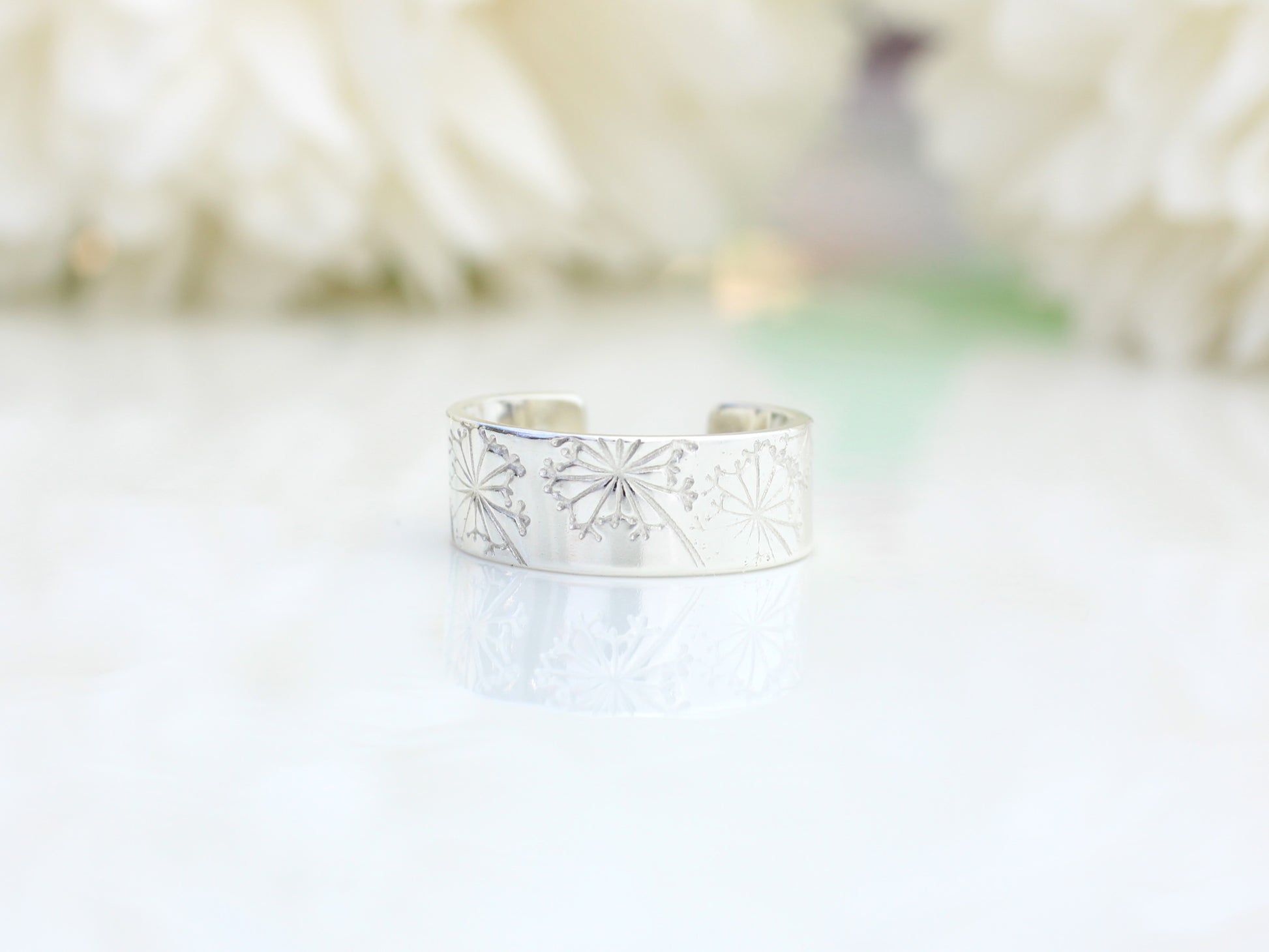 silver ear cuff with a dandelion design on a white surface