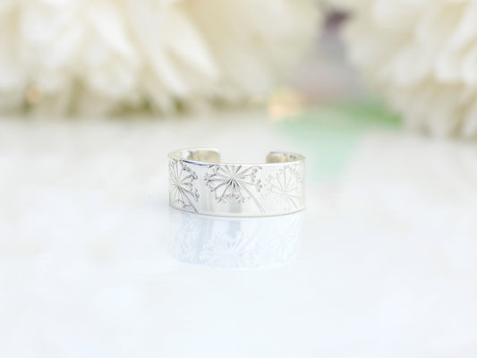 silver ear cuff with a dandelion design on a white surface