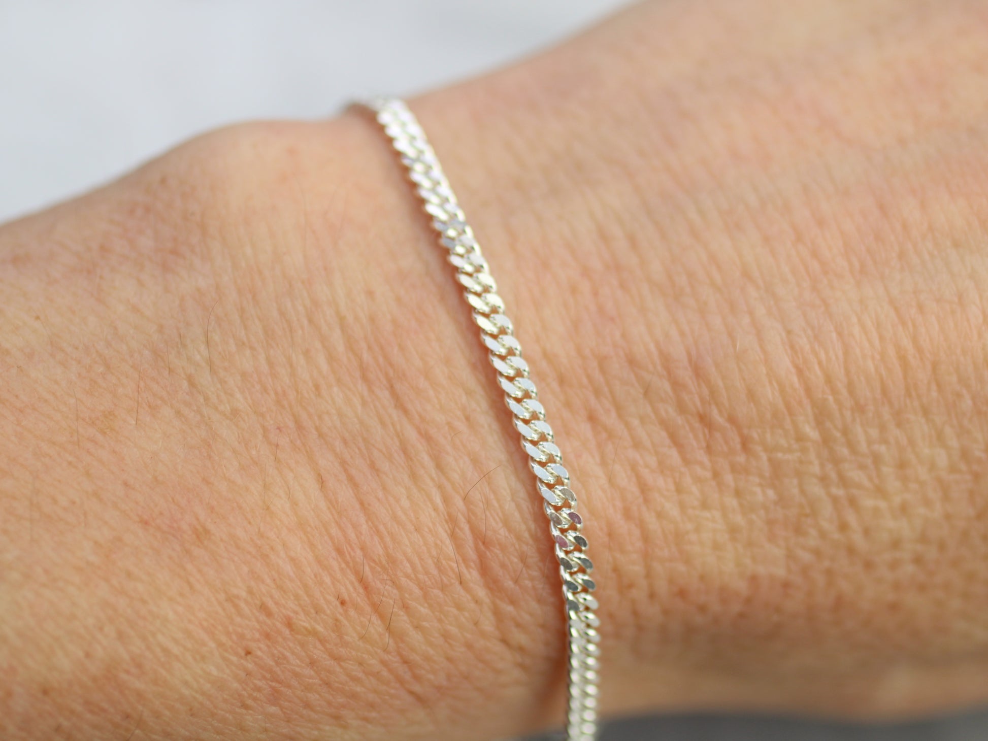 Silver bracelet on a wrist with a plain background
