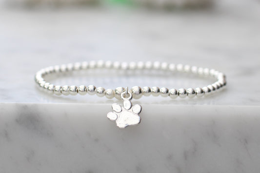 Silver beaded bracelet with a paw charm on a marble surface