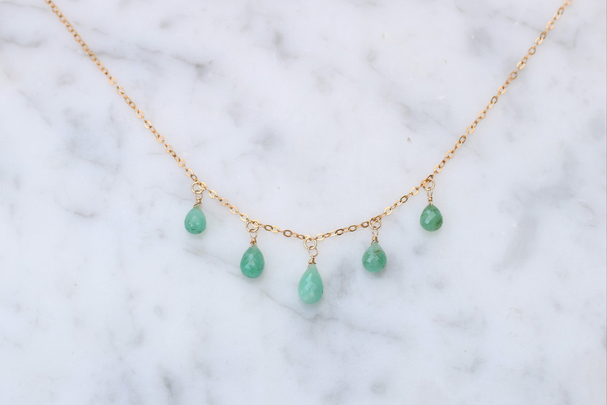 Gold necklace with green teardrop-shaped beads on a marble surface
