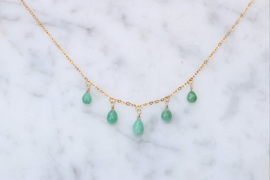 Gold necklace with green teardrop-shaped beads on a marble surface