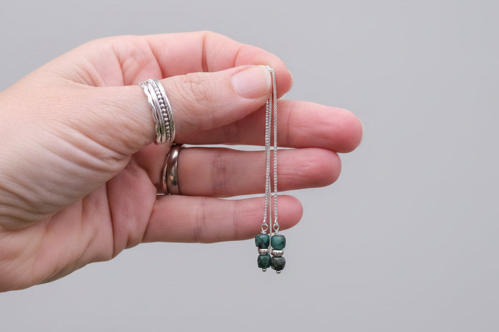 Hand holding emerald threader earrings with sterling silver threads and green emerald cube gemstones.