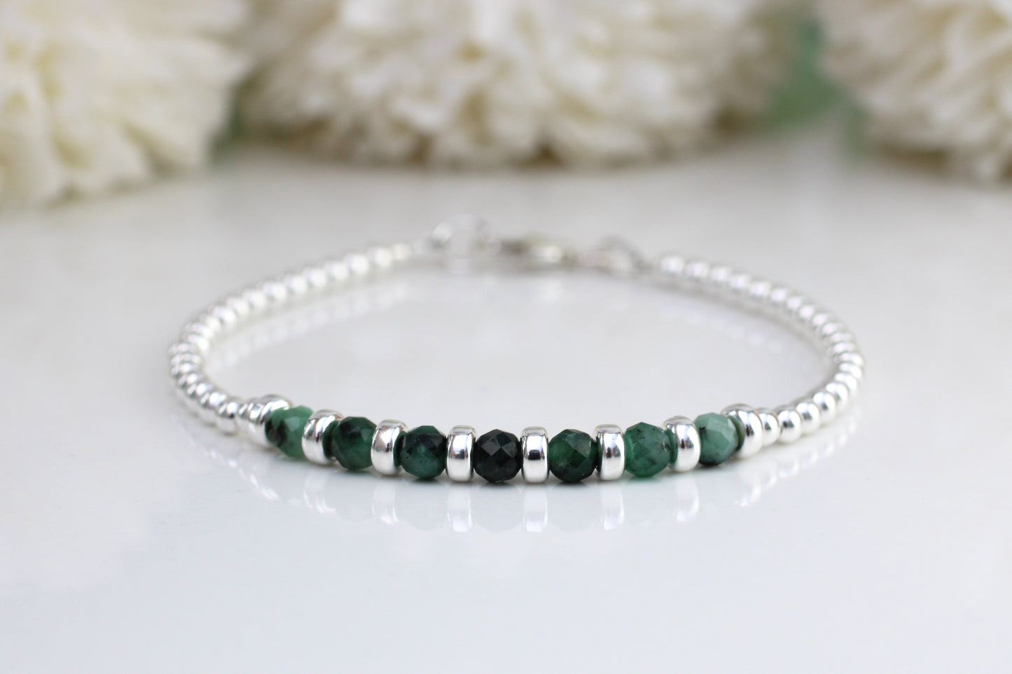 A sterling silver bracelet with green emerald gemstones, displayed against a white background with a floral pattern.