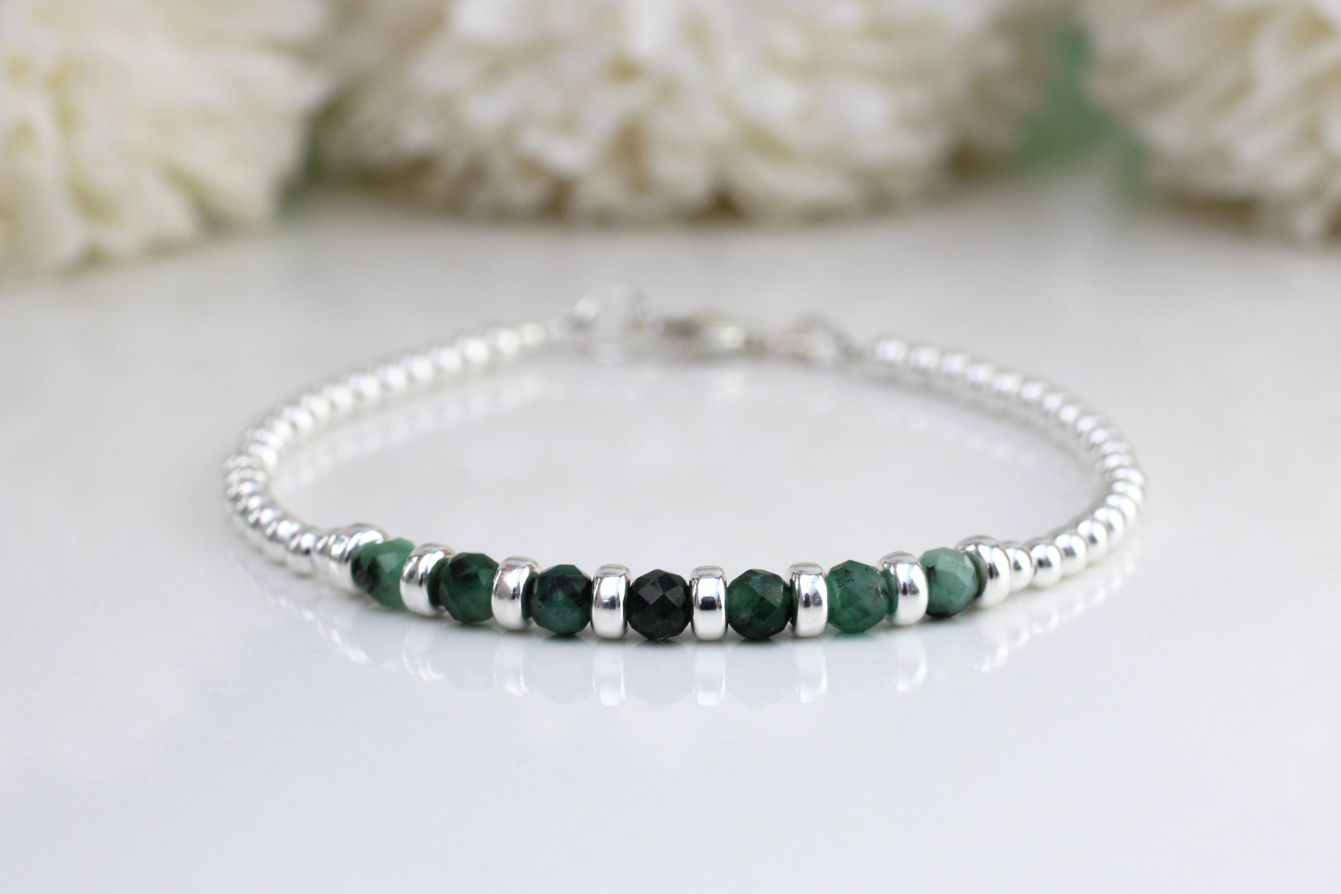 A sterling silver bracelet with green emerald gemstones, displayed against a white background with a floral pattern.