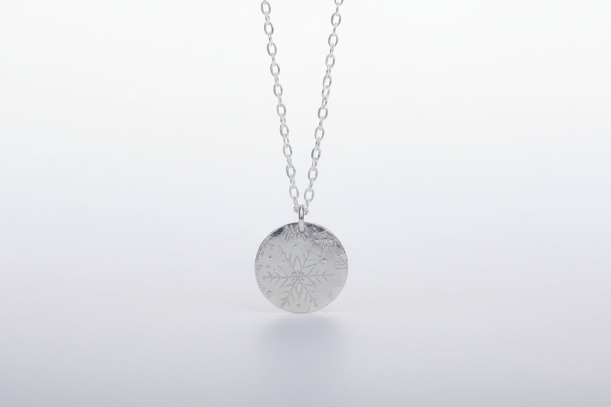Silver necklace with a snowflake pendant on a marble surface with a blurred floral background
