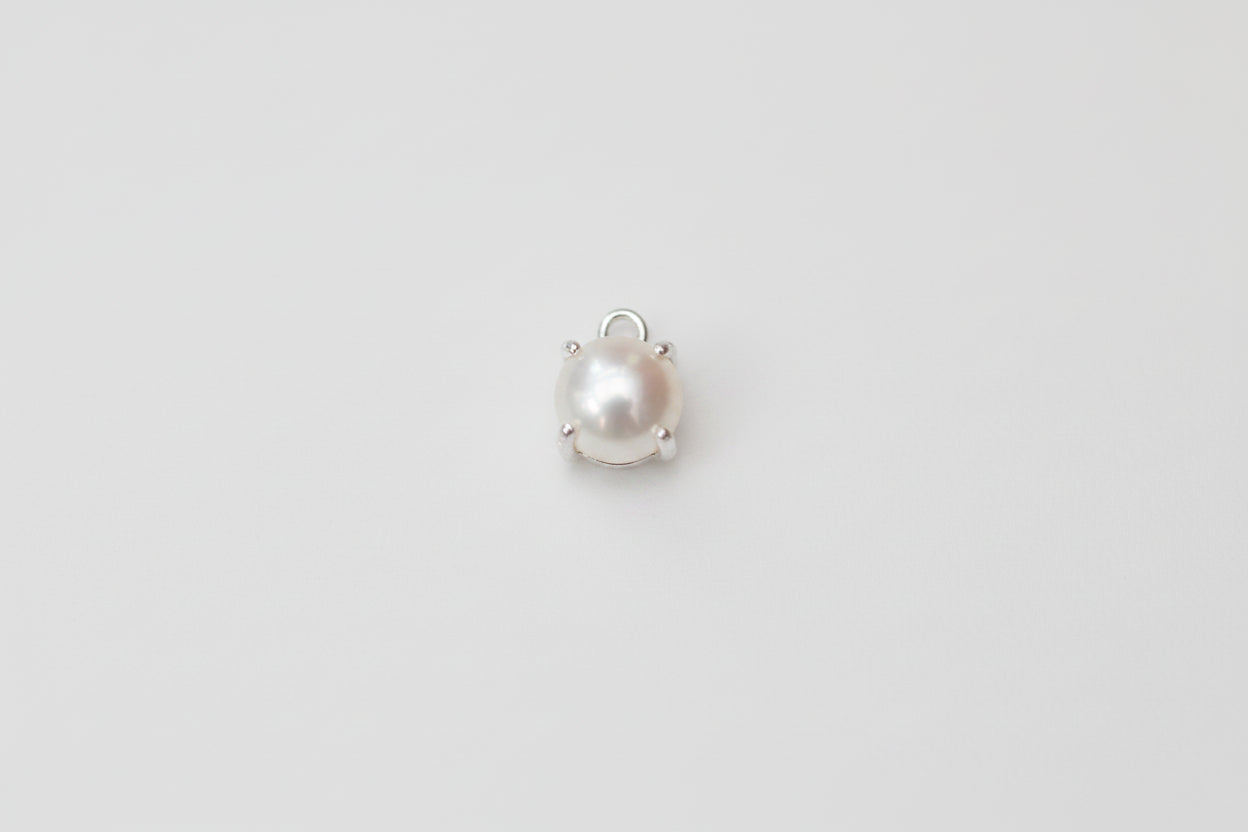 A single small pearl cabochon in a silver prong setting, displayed on a light gray and white marble surface.