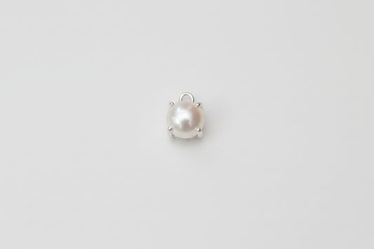A single small pearl cabochon in a silver prong setting, displayed on a light gray and white marble surface.