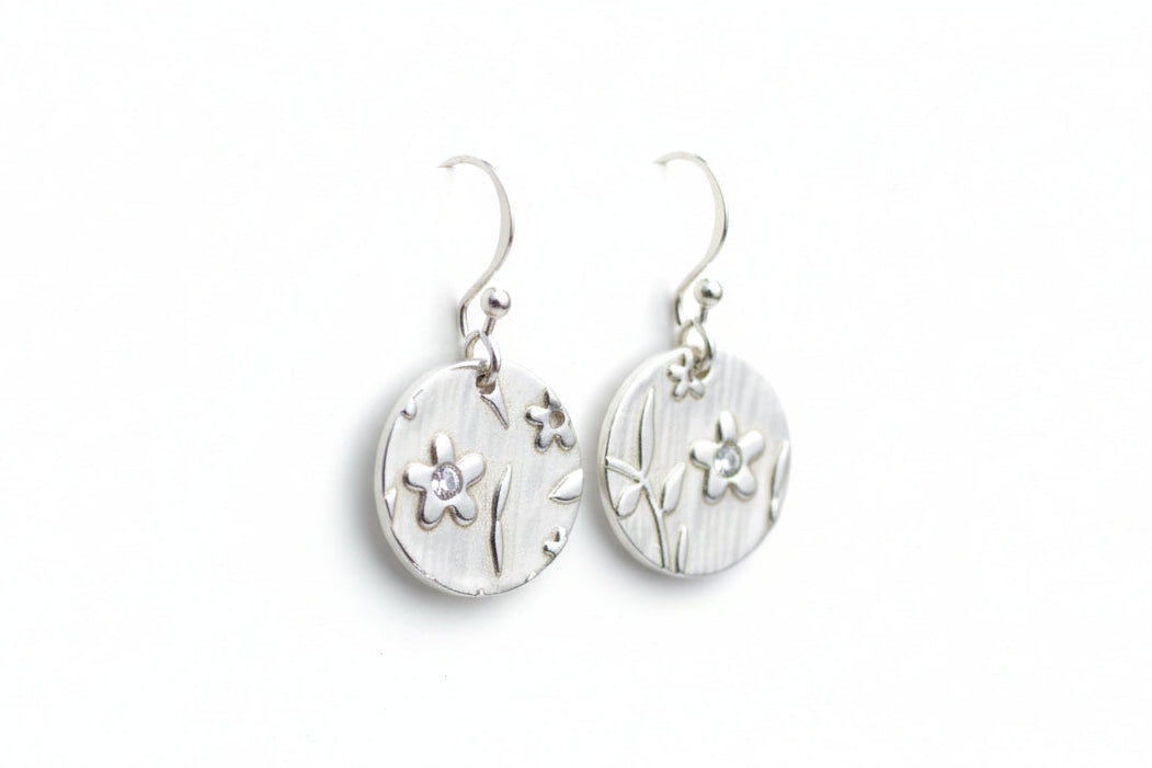 Pair of silver earrings with floral designs on a white surface