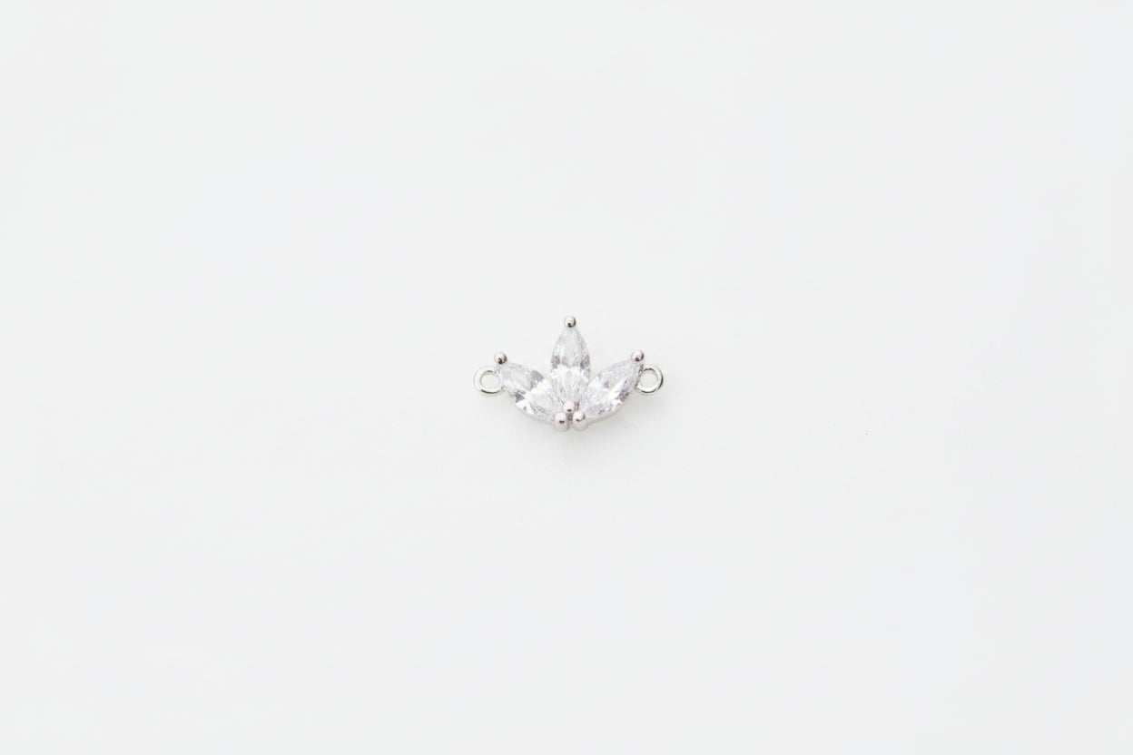 A small silver crown charm with clear rhinestones, displayed on a white marble surface.