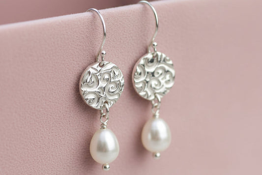 Silver earrings with pearl drops on a white cup