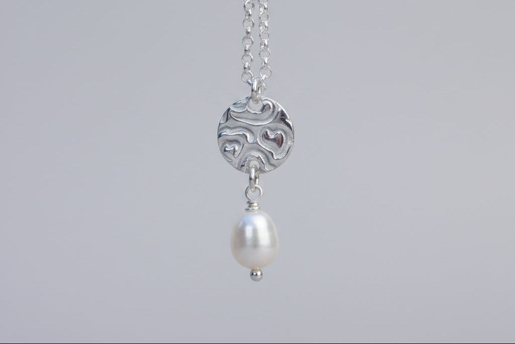 Silver necklace with a pearl pendant against a white floral background