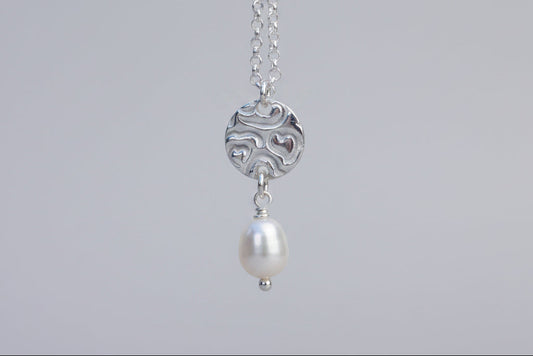 Silver necklace with a pearl pendant against a white floral background