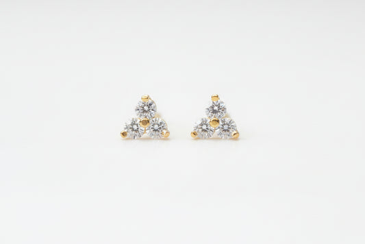 A pair of small triangular stud earrings with clear gemstones and gold-tone accents, resting on a light marble surface.