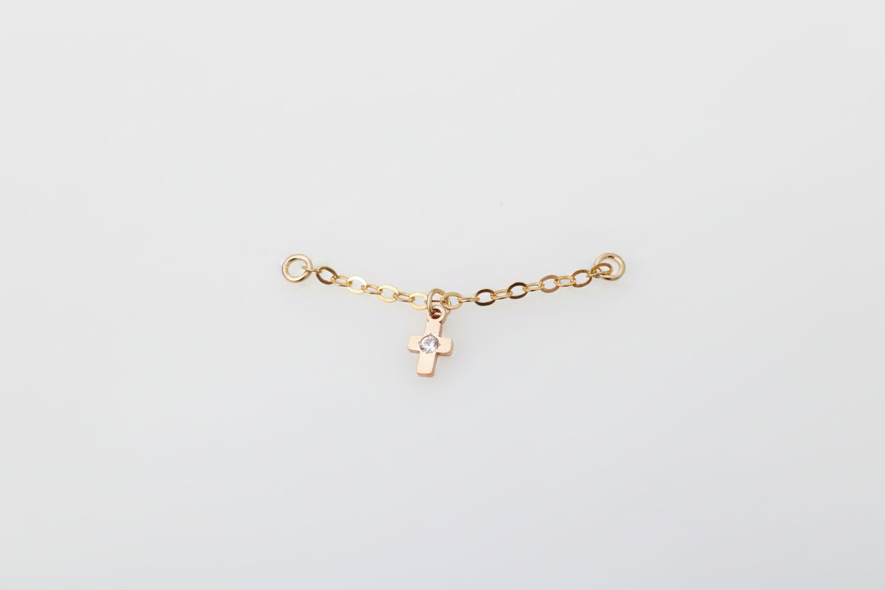 Gold ear chain with a cross charm on a marble background