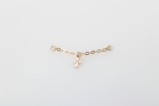 Gold ear chain with a cross charm on a marble background