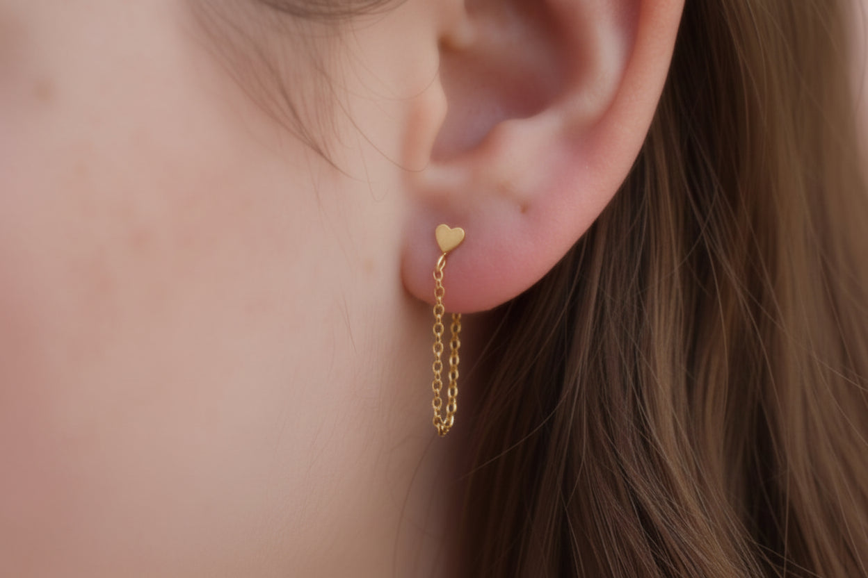 Gold heart-shaped earring worn on an ear with a blurred background